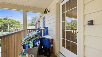 A covered porch with a wooden railing, a trash bin, and a storage unit with various items.