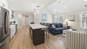 A modern kitchen with white cabinets, a large island, and a dining area with a blue sofa and striped armchair.