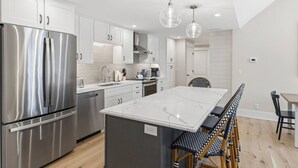 A modern kitchen with stainless steel appliances, a marble island, and a dining area with a bench and chairs.