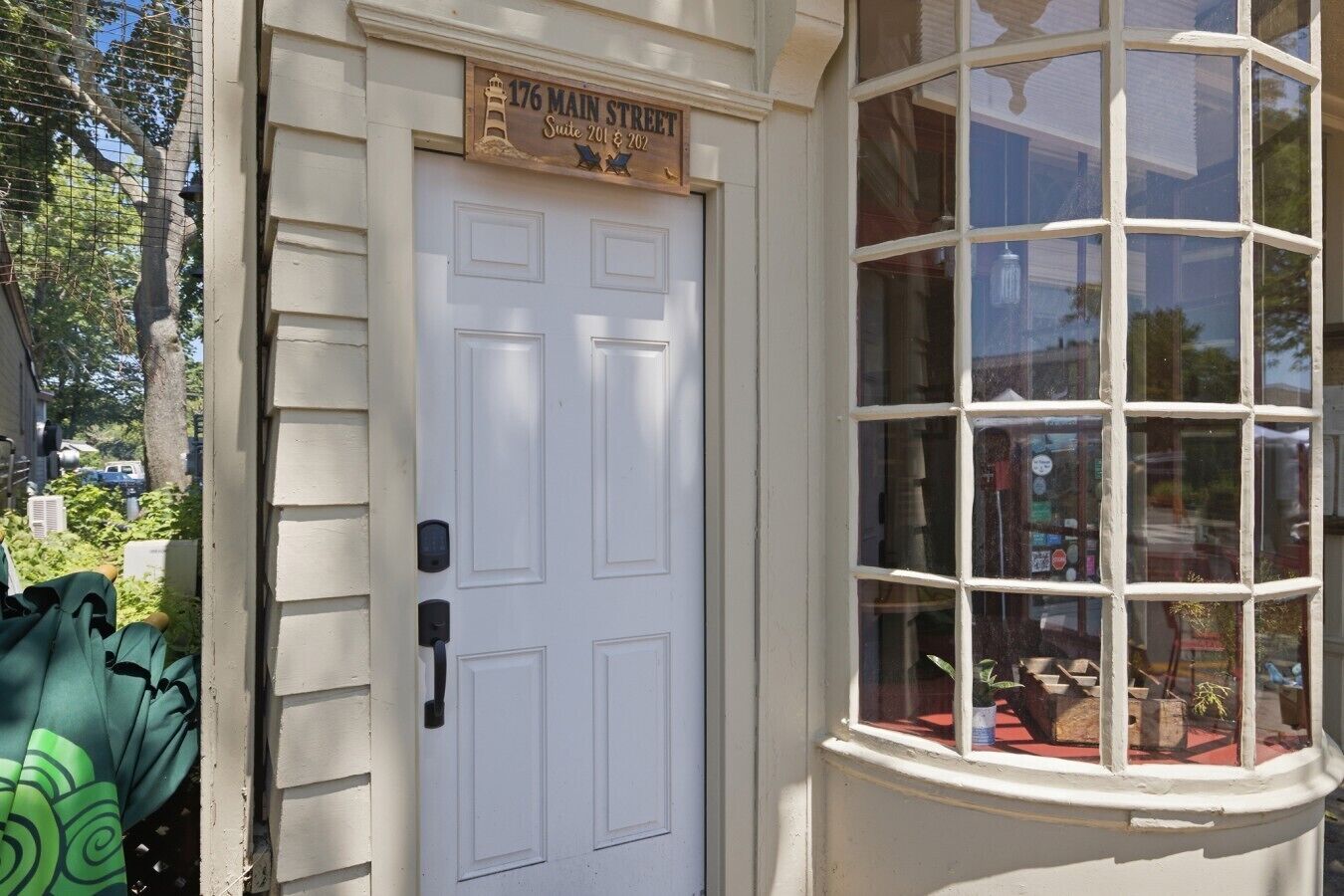 A white door with a sign above it, a window with multiple panes, and a small balcony area with plants.