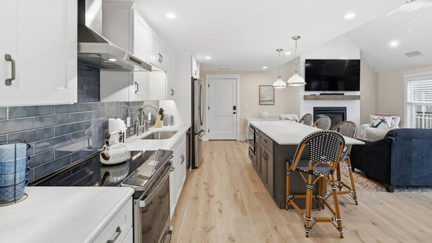Una cucina moderna con mobili bianchi, un'isola centrale e un'area pranzo con sedie in vimini.