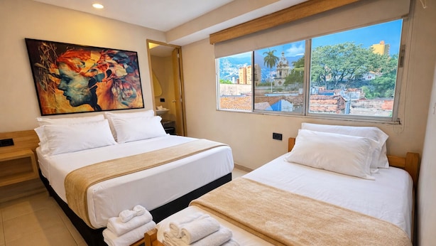 Habitació d'hotel amb dos llits, una finestra gran que dona a una vista de la ciutat i un quadre a la paret.
