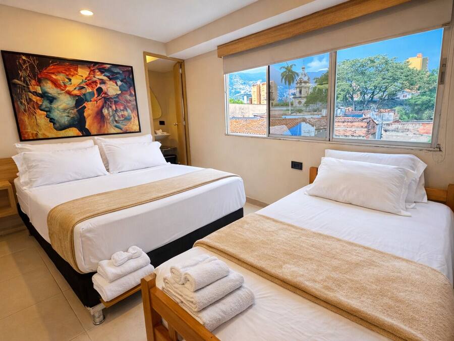 Habitación de hotel con dos camas, un ventanal con vistas a la ciudad y un cuadro en la pared.