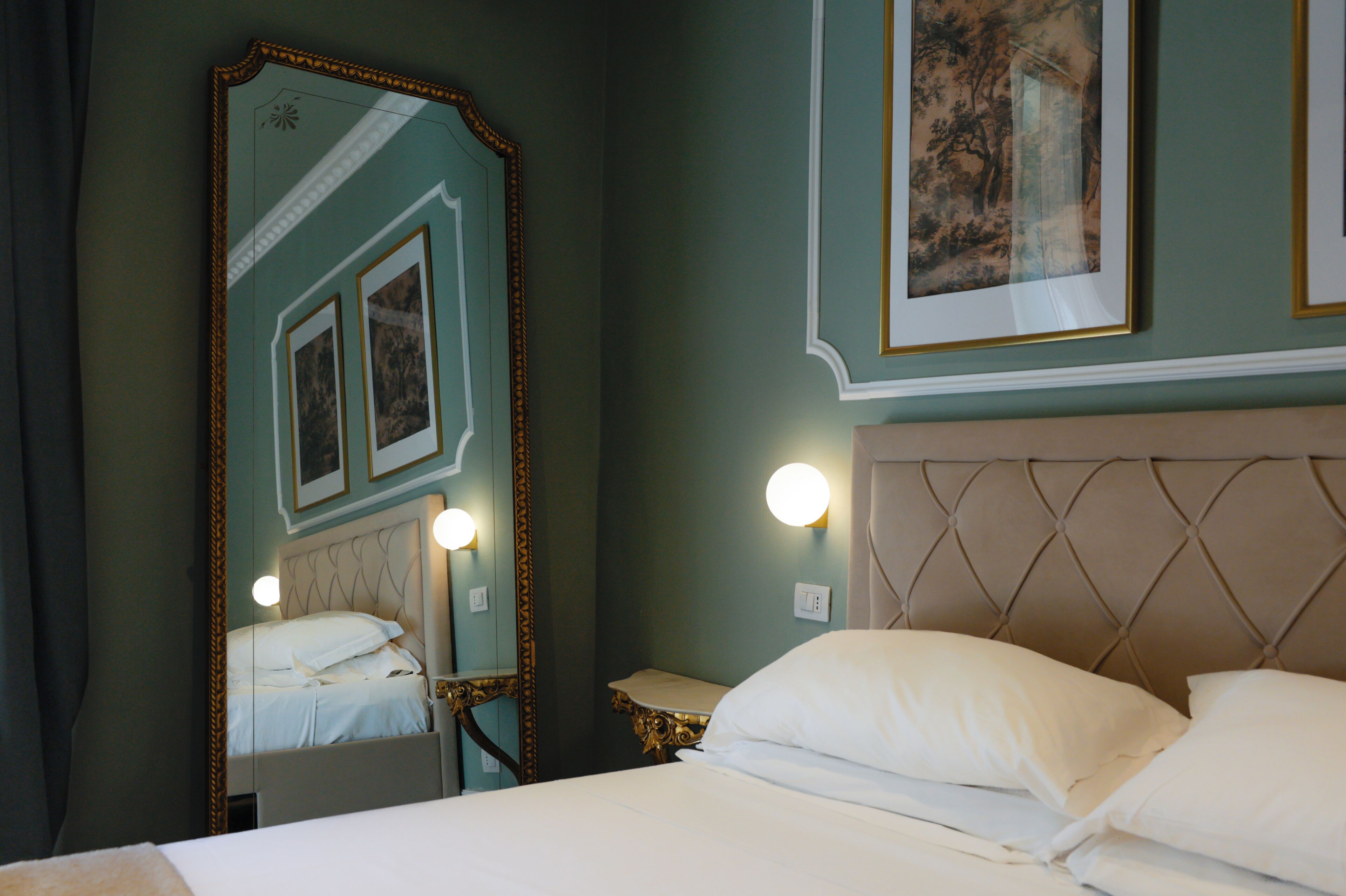A hotel room with a bed, a large mirror, a headboard, and wall-mounted lights.