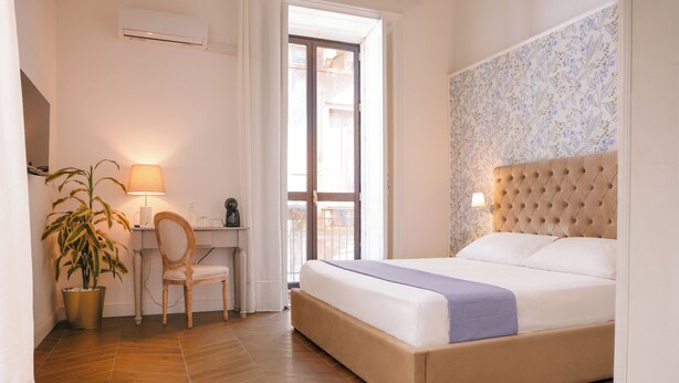 A bedroom with a bed, a desk with a chair, a potted plant, and a window. - BERETTI HOME (Catania)