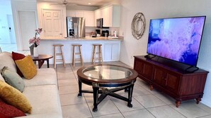 A living room with a sofa, a glass coffee table, a TV, and a kitchen in the background. - SWFL: Cape Coral Relax - Entire Home! (Cape Coral)