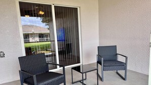 A patio with two chairs and a small table, a sliding glass door, and a concrete floor. - SWFL: Cape Coral Relax - Entire Home! (Cape Coral)