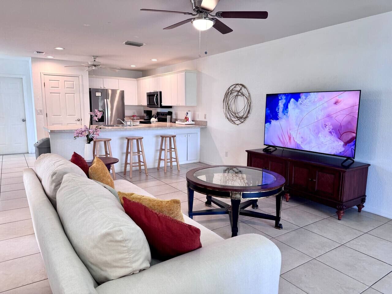Uma sala de estar moderna com sofá, mesa de centro, televisão e área de cozinha ao fundo.