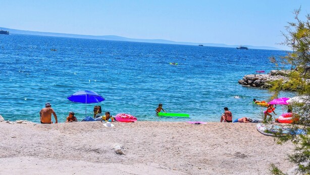 A beach with clear blue water, people swimming and sunbathing, and boats in the distance. - Marli Beach Apartments Jesenice Marli 1 (Dugi Rat)