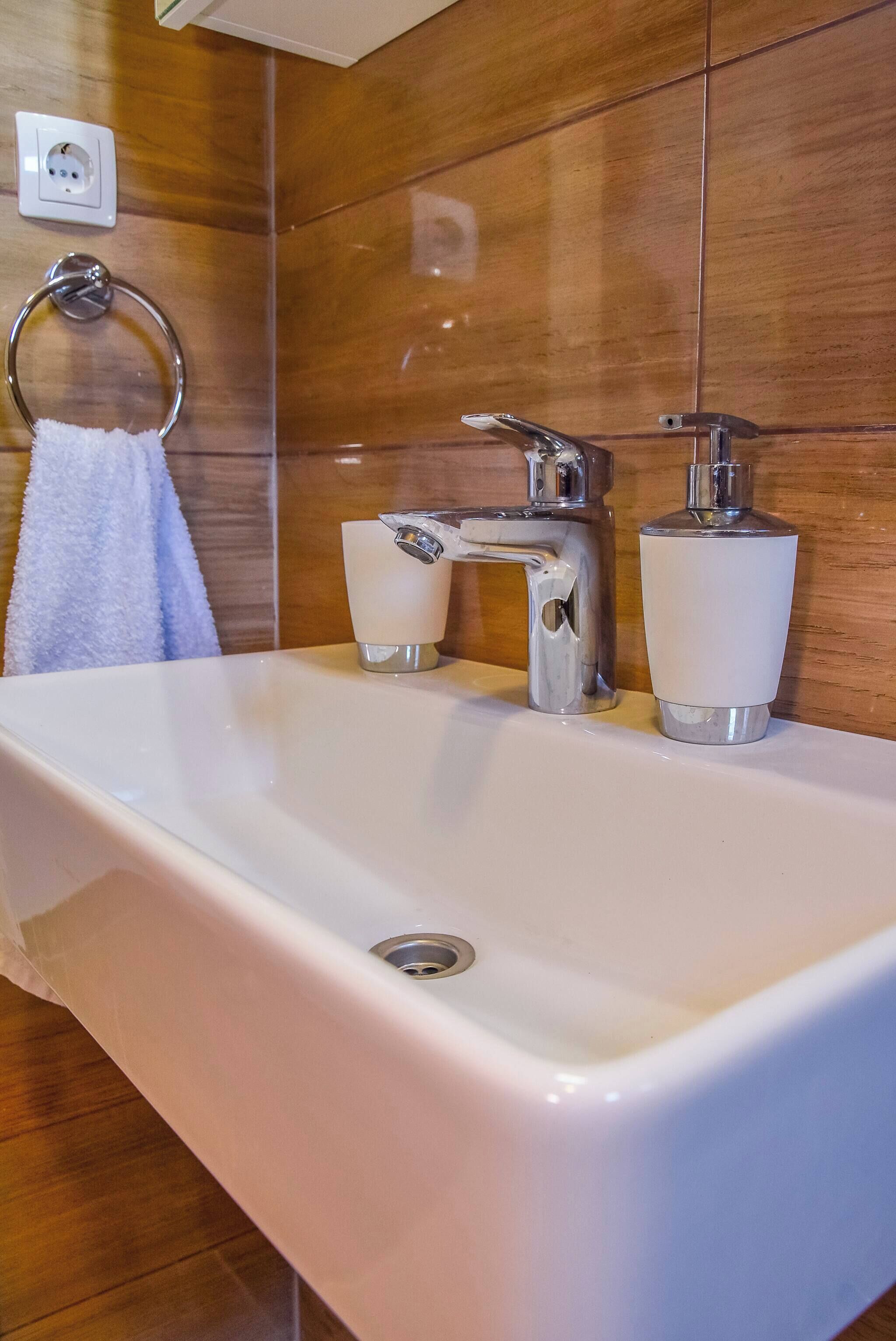A bathroom with a white sink, chrome faucet, and a soap dispenser.