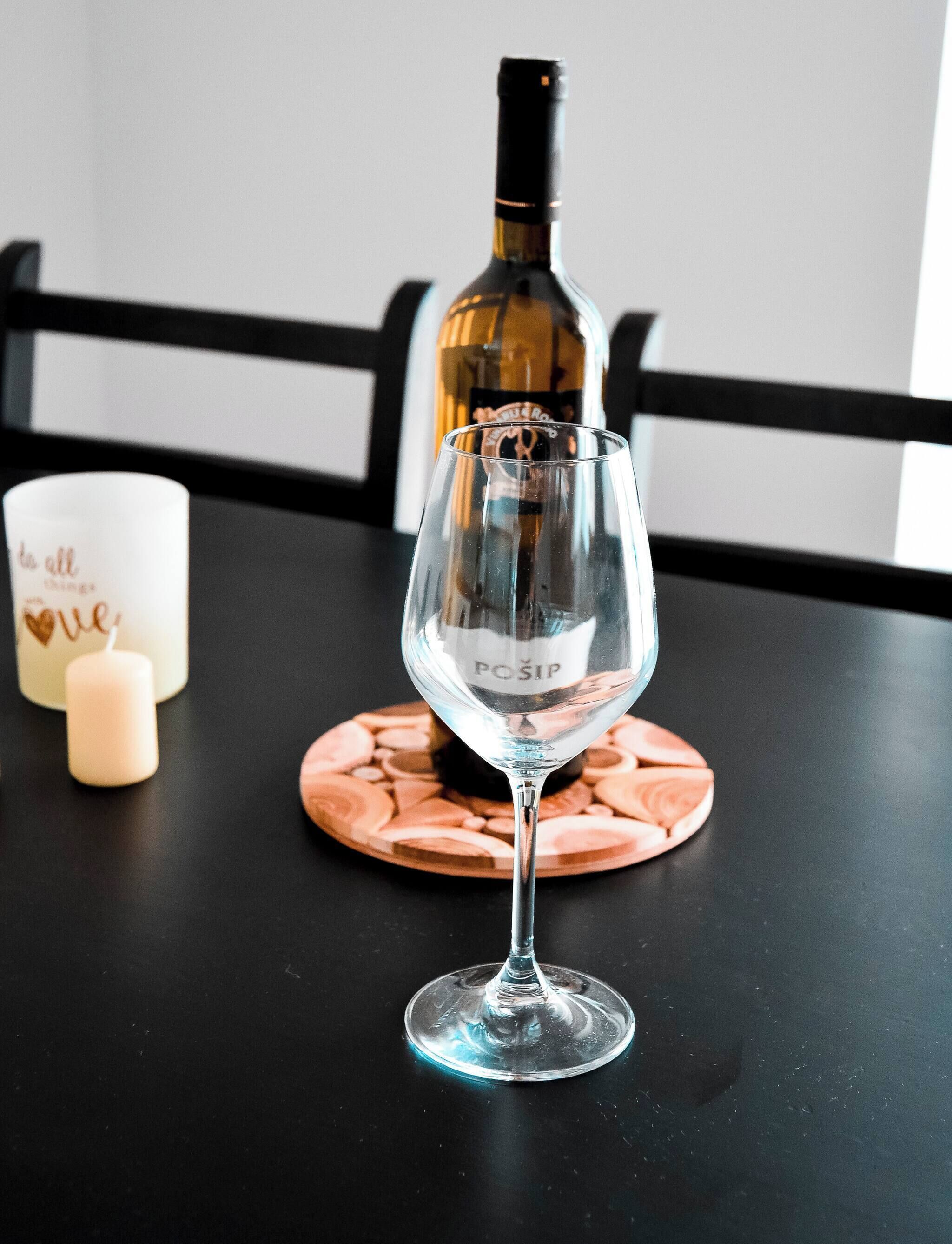 Un verre à vin posé sur un dessous de verre, une bougie et une bouteille de vin sur une table.