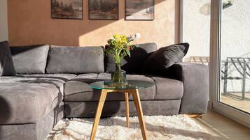 Ein modernes Wohnzimmer mit einem grauen Ecksofa, einem Glastisch und einem flauschigen weißen Teppich.