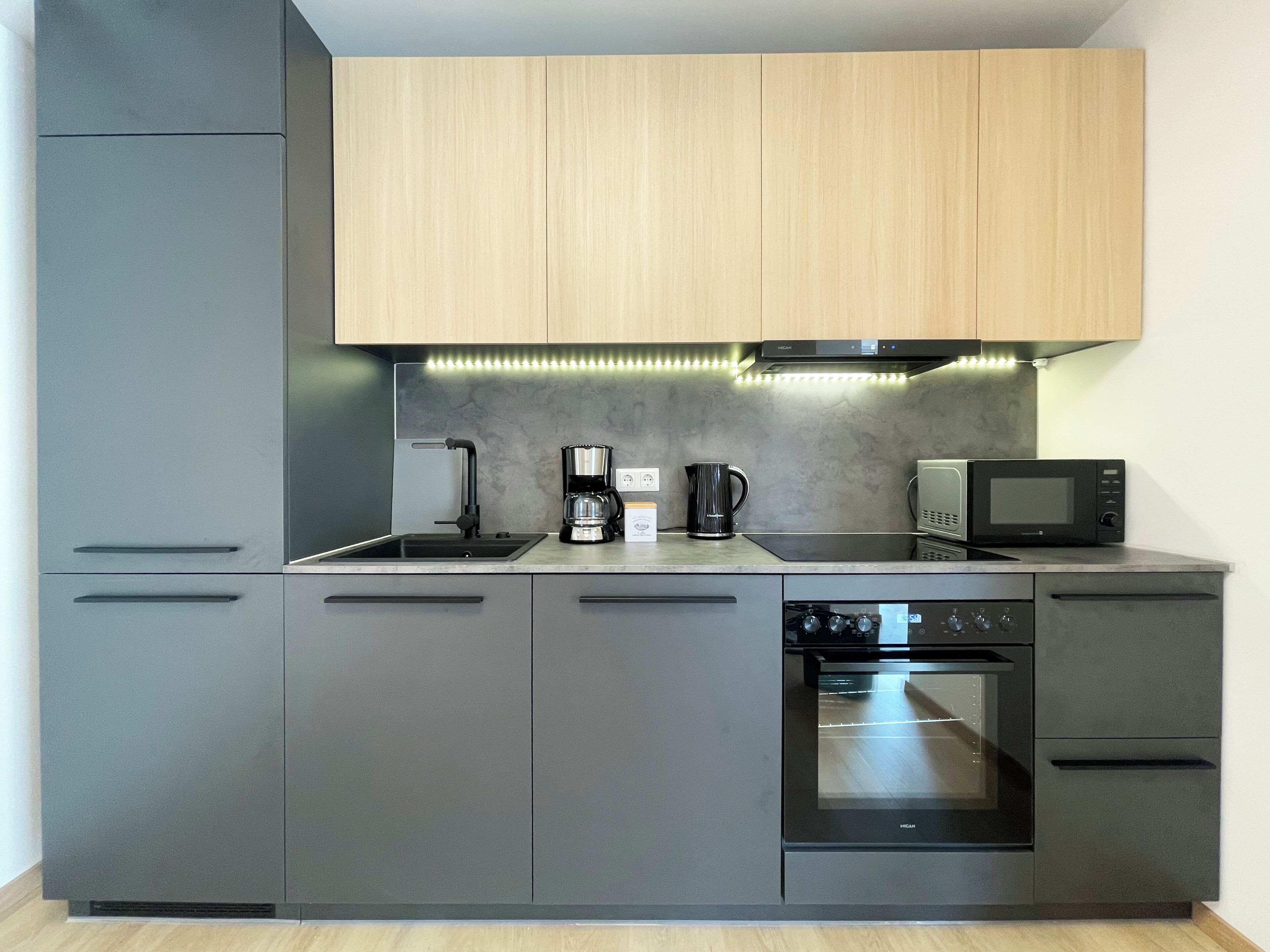 Eine moderne Küche mit grauen Schränken, einem Backofen, einer Mikrowelle, einer Kaffeemaschine und einem Spülbecken.