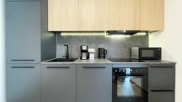 Eine moderne Küche mit grauen Schränken, einem Backofen, einer Mikrowelle, einer Kaffeemaschine und einem Spülbecken.