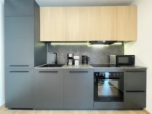 Eine moderne Küche mit grauen Schränken, einem Backofen, einer Mikrowelle, einer Kaffeemaschine und einem Spülbecken.