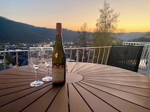 A bottle of Riesling Trocken on a wooden table with two glasses, overlooking a scenic view of a town and mountains at sunset. - Beautiful apartment Traumblick with balcony Bad Ems (Bad Ems)