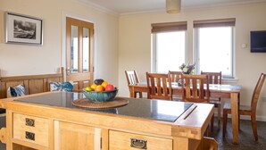 A kitchen with a wooden island, a dining table with chairs, a bowl of fruit, and a window with blinds. - Solas Alainn -  a detached house that sleeps 6 guests  in 3 bedrooms (Staffin)