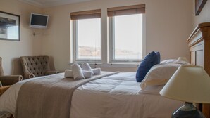 A hotel room with a bed, a chair, a TV, and a window with blinds. - Solas Alainn -  a detached house that sleeps 6 guests  in 3 bedrooms (Staffin)