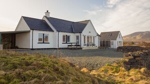 A white house with a dark roof, a covered porch, and a stone wall in the foreground.