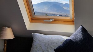 A room with a skylight, a bed with two pillows, a lamp, and a view of mountains.