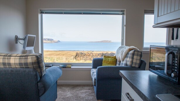 A cozy room with a view of the sea, a sofa, a chair, a small table, and a microwave.