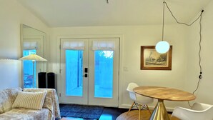 Uma sala de estar com sofá, mesa de centro, mesa de jantar com cadeiras, abajur e um quadro na parede.