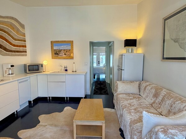 A compact living space with a kitchenette, a sofa, a coffee machine, and a refrigerator.