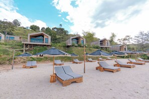Un resort frente al mar con sillas y sombrillas de madera, cabañas de madera con balcones y un cielo despejado.