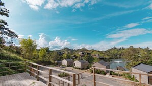 A wooden deck overlooking a lake with small cabins and a hilly landscape. - Okai by Bernalo Hotels (Guatape)