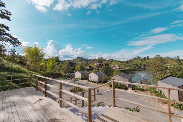 Une terrasse en bois donnant sur un lac, avec de petits chalets et un paysage vallonné.