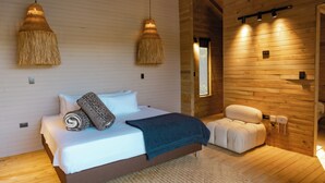 A wooden interior with a bed, two hanging lamps, a massage chair, and a wooden wall. - Okai by Bernalo Hotels (Guatape)