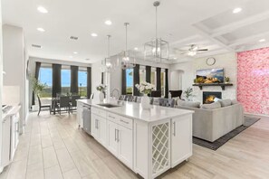 A modern kitchen with a central island, a dining area with a view, and a living room with a fireplace.