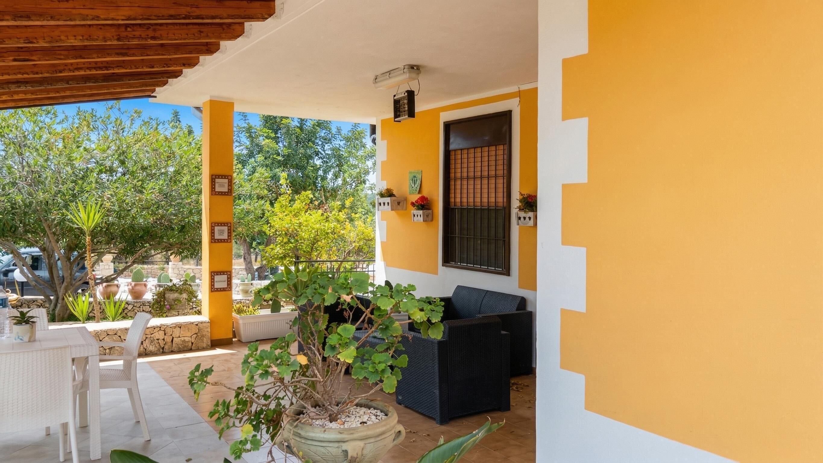Un patio cubierto con una mesa, sillas, plantas en macetas y un sofá negro.