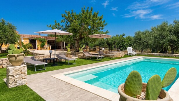 Zona de piscina con sillas de descanso, una maceta con cactus y un muro de piedra.