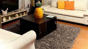 Sala de estar con sofá, una mesa de centro, televisor, chimenea y un mural de plantas tropicales.
