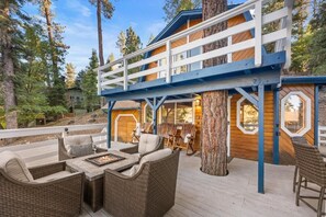 A two-story wooden cabin with a deck, wicker furniture, and a fireplace. - Deer Canyon Home (Big Bear Lake)