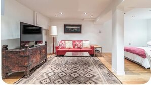 Une chambre moderne avec un canapé rouge, une télévision, un tapis à motifs et un lit.