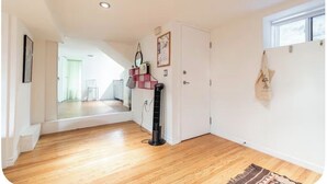 Un couloir avec un plancher en bois, une porte blanche, un miroir et un petit ventilateur.