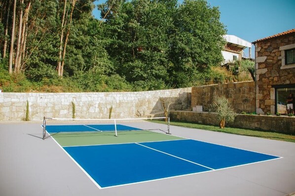 Un court de tennis en plein air, avec un mur en pierre et des arbres en arrière-plan.
