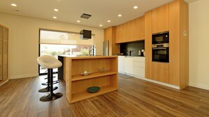 A modern kitchen with wooden cabinets, a built-in microwave, and a bar stool. - Sandoco House Golf Adventure (Ponte de Lima)
