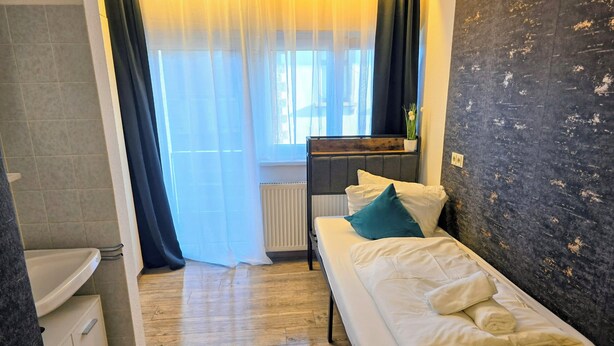 Un dormitorio pequeño y ordenado con una cama individual, una mesita de noche, un radiador y una ventana con cortinas.