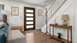Ein modernes Interieur mit einer Holztreppe, einer Bank, einem Konsolentisch mit Lampe und gerahmten Kunstwerken an den Wänden.
