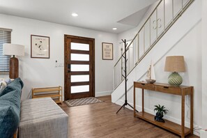 Ein modernes Interieur mit einer Holztreppe, einer Bank, einem Konsolentisch mit Lampe und gerahmten Kunstwerken an den Wänden.