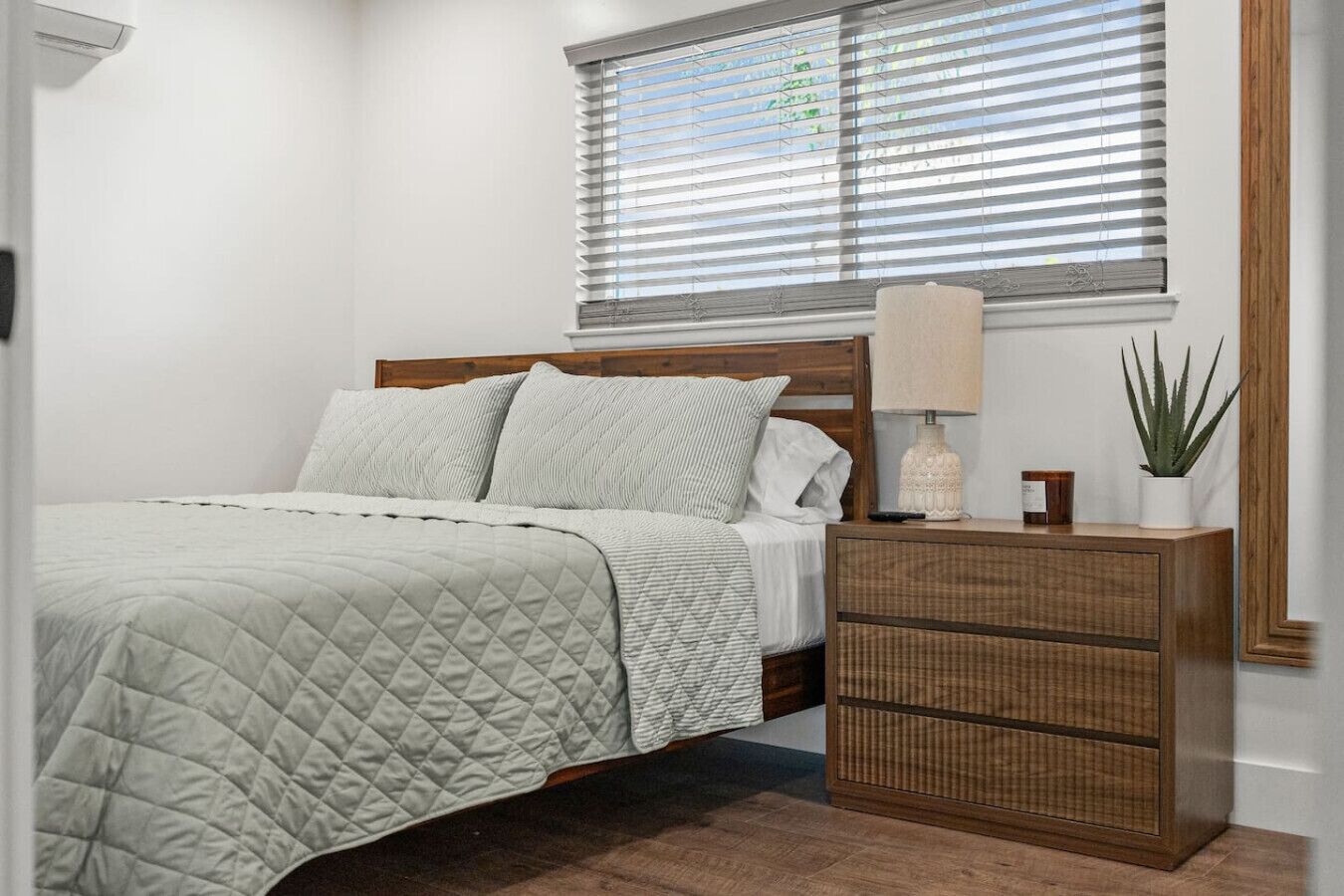 A bedroom with a bed, bedside table, lamp, and a potted plant.