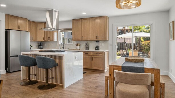Eine moderne Küche mit Holzschränken, einem Edelstahlkühlschrank und einer Bar mit zwei Hockern.