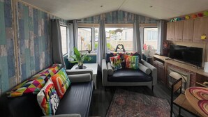 Interno compatto di un camper con divano, poltrona, tavolo da pranzo, televisore e mobili.