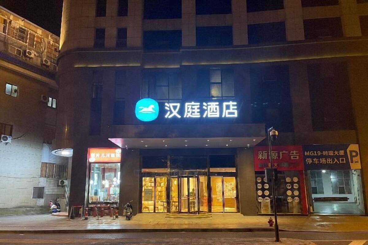 L’entrée d’un hôtel, avec une enseigne indiquant « 汉庭酒店 » et une porte d’entrée bien visible.