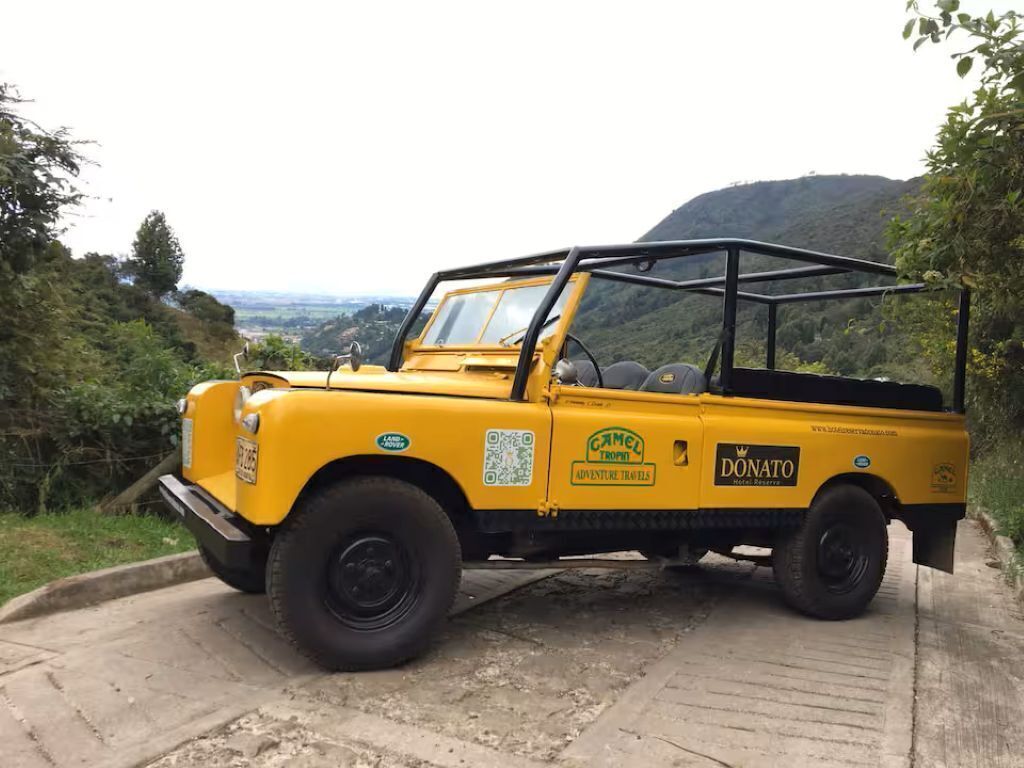 Un véhicule tout-terrain jaune est garé sur un chemin de béton, offrant une vue panoramique sur des collines et une végétation luxuriante en arrière-plan.