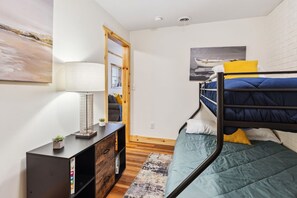 A compact bedroom with a bunk bed, a bedside table with a lamp, a small plant, and a painting on the wall.