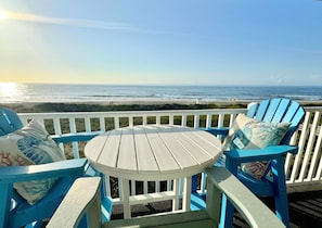 Une terrasse avec une table ronde et des chaises bleues, donnant sur une plage.